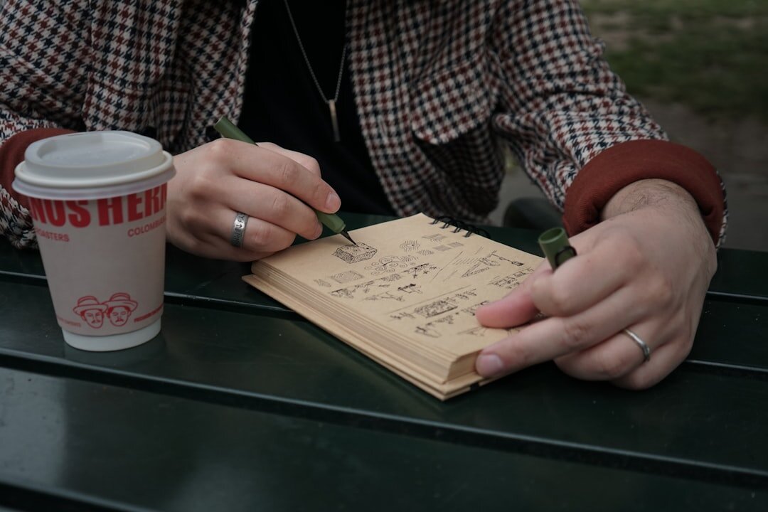 Close up of hands writing in a personal journal with a cup of coffee on a wooden table